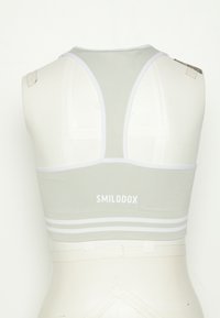 Sutiã desportivo verde claro com um design de costas nadador, apresentando uma borda e riscas brancas na parte inferior. Logótipo "SMILODOX" exibido em branco.