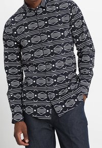 Zwarte overhemd met knopen, voorzien van een geometrisch wit patroon van diamanten, lijnen en cirkels. Gemaakt van katoen met een standaard kraag en lange mouwen.