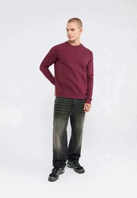 Burgunderfarget sweatshirt med lange ermer og rund hals, kombinert med mørkegrå denimjeans og svarte treningssko med teksturerte såler.