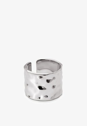Strieborný kovový prsteň s textúrovaným, kladivkovým povrchom, ktorý má nepravidelné vzory a otvorený dizajn na zadnej strane.