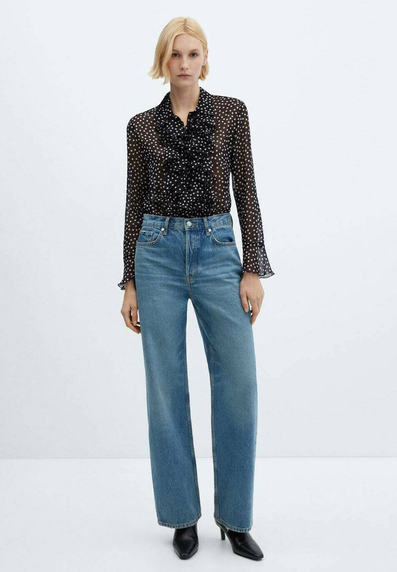 Schwarze transparente Bluse mit weißen Punkten, geraffter Vorderseite und langen Ärmeln, kombiniert mit hoch taillierten, hellblauen geraden Jeans und schwarzen Stiefeln.