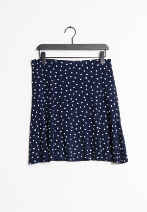 Granatowa spódnica w białe kropki zawieszona na czarnym wieszaku na białym tle.