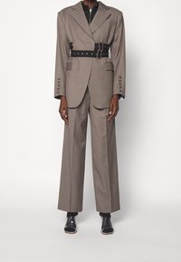 Brun skräddarsydd blazer med ett åtdraget svart bälte, vida byxor och klara klackskor. Texturerat tyg och strukturerade designdetaljer.