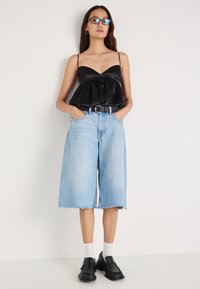 Czarny satynowy top na cienkich ramiączkach z marszczonym przodem, zestawiony z jasnoniebieskimi denimowymi culottes z postrzępionym wykończeniem i kieszeniami. Czarne buty.