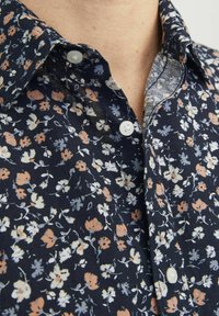 Camicia floreale navy con un motivo in scala ridotta in crema, pesca e blu, con colletto a punta e bottoni bianchi. Tessuto strutturato.