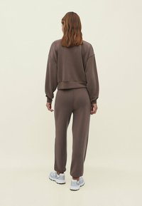 Bruine sweatshirt en trainingsbroek in een zachte textuur, met een relaxte pasvorm, schoudervallen en elastische boorden, gecombineerd met grijze sneakers.