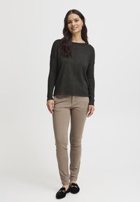 Pull en maille texturée vert foncé avec un décolleté large, associé à un pantalon ajusté beige et des mocassins noirs avec des accents dorés.