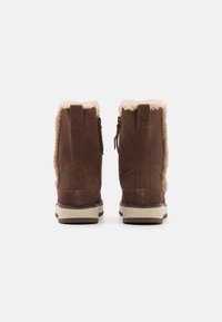 Brown suede ankle boots with faux fur lining and side zippers. Flat soles with a contrasting tan trim. Simple, rounded design for warmth.