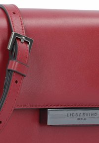 Red leather handbag with smooth texture, rectangular shape, and silver hardware strap. Features a logo plaque and contrast stitching.