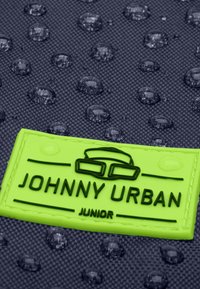 Fekete, textúrált felület vízcseppekkel. Sárgászöld logópanel "JOHNNY URBAN JUNIOR" szöveggel és szemüveg grafikával.