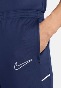 Marineblauwe sportshorts van ademend materiaal, met een zijrits zak en een wit Nike-logo op de dij gestikt.