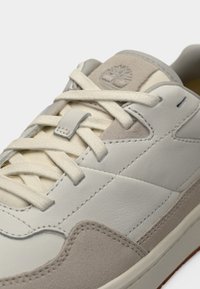 Λευκό και ανοιχτό γκρι αθλητικό παπούτσι με δερμάτινα και σουέντ υλικά, επίπεδα κορδόνια, ένα ετικέτα με λογότυπο και υφασμένη ελαστική σόλα.