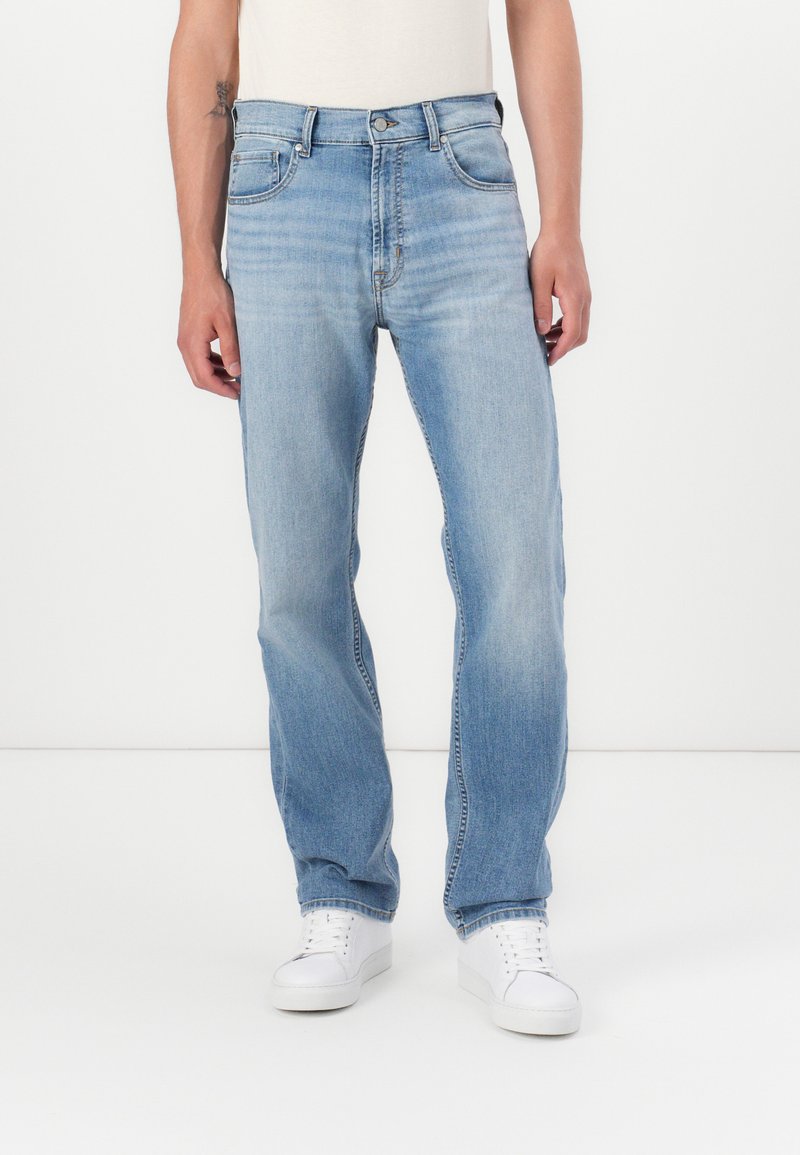Jeans de mezclilla azul claro con corte recto, diseño de cinco bolsillos y un ligero desvanecimiento. Combinados con zapatillas blancas.