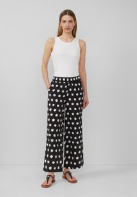 Pantalons larges noir et blanc à pois avec une taille élastique et des poches latérales, associés à un débardeur blanc ajusté et des sandales.