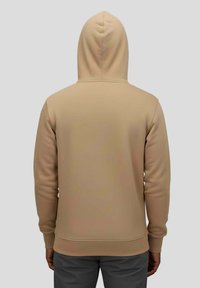 Sweat à capuche beige à coupe décontractée, avec capuche à cordon, poignets et ourlet côtelés, et texture lisse, présenté de dos.