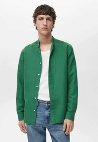 Green button-up shirt in breathable fabric, featuring a band collar, long sleeves, and white buttons, paired with light blue jeans.