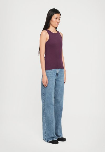 Paarse aansluitende tanktop gecombineerd met losse blauwe denim jeans, met een hoge taille en wijde pijpen, gedragen met zwarte schoenen.