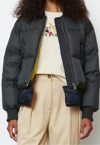 Black puffer jacket with quilted texture, zip closure, and ribbed cuffs. Features side pockets and a yellow inner lining.