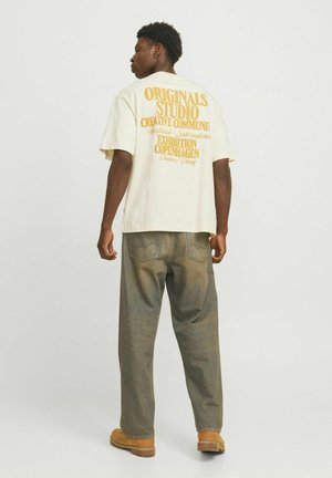 Short-sleeve, cream t-shirt with bold yellow text on the back. Paired with loose, faded denim jeans and brown boots.