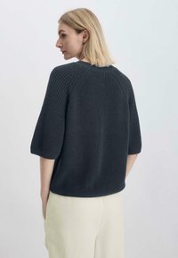 Tumma harmaa neulepaita jossa on lyhyet hihat ja teksturoitu ribbikuvio. Rentoa istuvuutta, pyöreä pääntie ja roikkuneet olkasaumat.