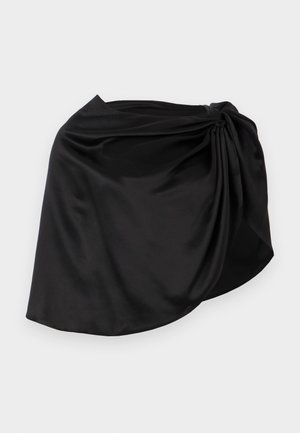 Μίνι φούστα από μαύρο σατέν με ασύμμετρο τελείωμα και συγκέντρωση υφάσματος στη δεξιά πλευρά, σε απλό φόντο.