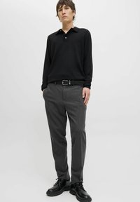 Camisa polo negra de manga larga con collar, combinada con pantalones de traje grises y botas negras de cordones. Tela suave y diseño ajustado.