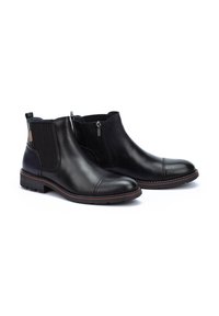 Botas de tobillo de cuero negro con un acabado suave, punta redondeada, cremallera lateral, paneles elásticos y detalle de suela marrón en contraste.