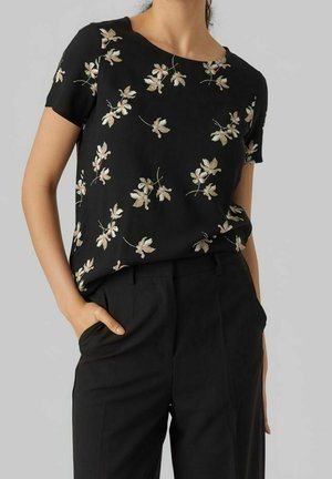 Top nero a maniche corte con un motivo floreale totale in beige e verde, con scollatura a girocollo, abbinato a pantaloni neri sartoriali.