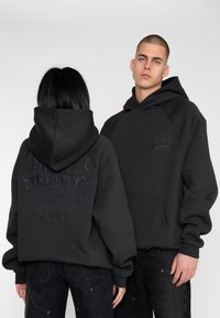 Black hooded sweatshirt with a front pocket and embroidered logo on the chest. Features a large logo on the back, made of soft material.