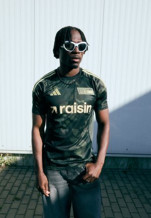 Zelena kamuflaža Adidas majica s žutim naglascima i logotipom, uparen s sivim trapericama. Nosim bijele sunčane naočale i crnu ogrlicu.