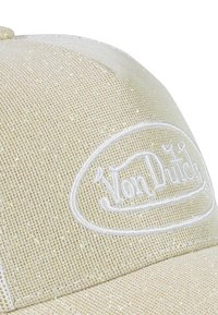 Gorra de béisbol de malla color arena con el logo bordado en blanco de "Von Dutch". La textura es fina con un sutil brillo, complementada por una corona estructurada.