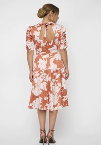 Blumen-Midikleid in rostorange mit weißen Mustern, kurzen Puffärmeln, Rückenschlitz und Bindeband. Glatte, weiche Textur.