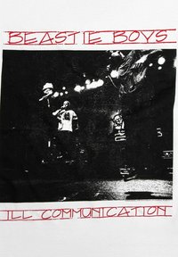 Bílý tričko s černou grafikou vystupujících umělců na scéně, s nápisy "BEASTIE BOYS" a "ILL COMMUNICATION" v tučném červeném písmu nad a pod grafikou.