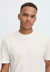 Camiseta de algodón color beige claro con cuello redondo y mangas cortas, que presenta una textura suave y un diseño clásico y sencillo.