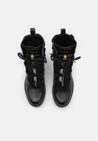 Bottes à lacets en cuir noir avec détails de fermeture éclair dorée, semelles plates et accents de logo bien visibles, dotées d'un bout rond et de panneaux texturés.