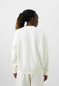 Hvid crewneck sweatshirt med lange ærmer, lavet af blødt materiale. Ribbet kant og manchetter. Glat tekstur, minimalistisk design.