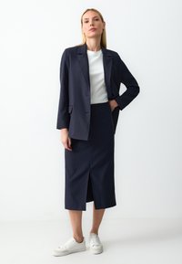 Marineblauw pinstripe blazer en rok set, met een slit aan de voorkant van de rok, gecombineerd met een witte top en witte sneakers. Zachte stoftextuur.