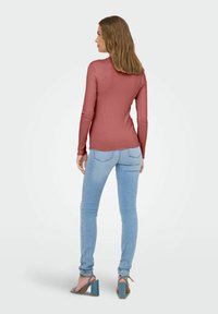 Top a maniche lunghe in jersey a coste rosa antico, con colletto alto e orlo curvo, abbinato a jeans skinny azzurri e sandali con tacco largo.
