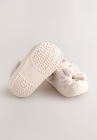 Lyse beige slip-on sko med blødt faux pelsdetalje, tekstureret gummisål og ventilationshuller for åndbarhed. Rundet form for komfort.