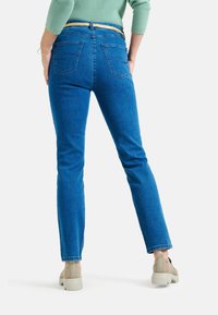 Jeans in denim blu con vestibilità dritta, cinque tasche e una cintura marrone chiaro. Il tessuto appare morbido con una leggera elasticità e una minima scoloriture.