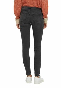 Svarta skinny jeans i denim, med en midjehöjd och en slät yta. Två bakfickor synliga, tillsammans med vita sneakers.