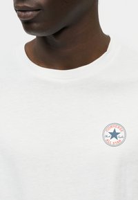 Λευκό φούτερ με στρογγυλή λαιμόκοψη και κεντητή λεπτομέρεια με το λογότυπο "Converse All Star" σε κόκκινο και μπλε στο στήθος. Μαλακή υφή βαμβακιού.