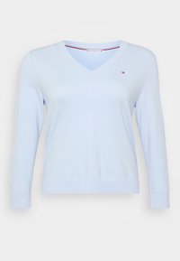 Lyseblå v-hals genser med lange ermer, ribbestrikkede mansjetter og kant. Laget av et mykt materiale, med en liten logo på venstre bryst.