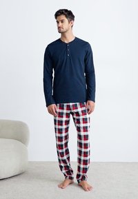 Langsleeve marineblauw top met knoopsluiting, gecombineerd met geruite pyjamabroek in rood, zwart en wit. Zacht materiaal, relaxte pasvorm, casual ontwerp.