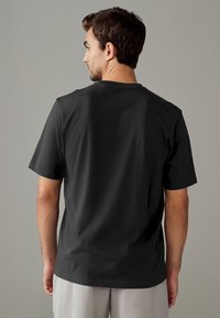 T-shirt nera in cotone con maniche corte, scollo rotondo e texture liscia. Vista posteriore mostra una vestibilità comoda e nessun marchio visibile.