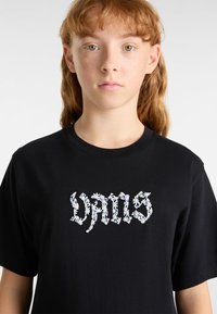 Zwarte katoenen t-shirt met geborduurde witte bloemletters op de voorkant. Ronde hals en korte mouwen met een ontspannen pasvorm.