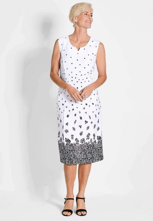 Weißes ärmelloses Kleid mit schwarzen Blumenmustern, V-Ausschnitt, schwarzem ornamentalen Saum am unteren Rand und gerader Silhouette.