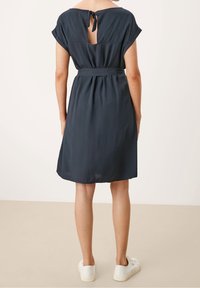 Marinblå klänning med bälte och korta ärmar, med en öppenhet bak på ryggen, tillverkad av lätt material, med en avslappnad passform och slät textur.