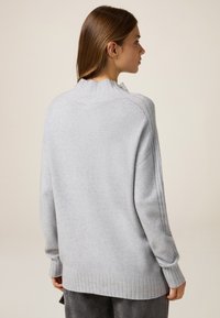 Maglione oversize grigio chiaro con orlo e polsini a costine. Presenta un colletto alto e sottili cuciture verticali sulle spalle. Tessuto morbido.
