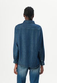 Denim overhemd in donkerblauw, met lange mouwen, knopenmanchetten en een losse pasvorm, voorzien van een puntige kraag en zichtbare stiksels.